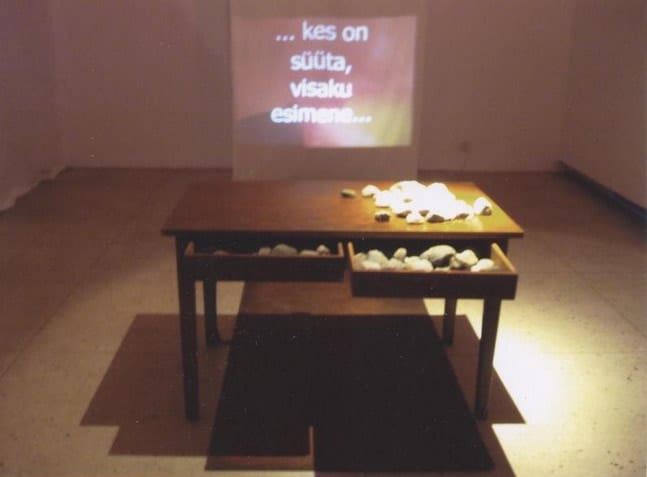 "KES SÜÜTA, VISAKU ESIMENE KIVI..." 2003 installatsioon: laud, kivid, video <br /> "WHO IS INNOCENT, ...." 2003 installation: table, stones, video